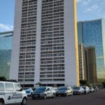 Edifício do Hotel Torre Palace em Brasília com barreiras e viaturas de segurança para implosão, em estilo fotojornalístico.
