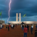 Raio atingindo área de manifestação política em Brasília, com céu tempestuoso e veículos de emergência ao fundo.