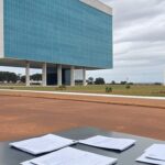 Edifício da Caesb em Brasília com documentos de concurso e relógio indicando prazo apertado, destacando falhas potenciais.