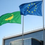 Bandeiras da UE e Mercosul em edifício no Brasil, representando acordo histórico de livre-comércio com PIB de US$ 22 trilhões.