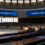 Sala de sessões vazia da CLDF em Brasília, com microfones e telas de transmissão ao vivo, representando estagnação em debates legislativos.