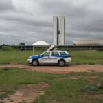 Viatura da polícia legislativa em rua de Brasília com cena de crime ao fundo, destacando escalada de violência no DF.