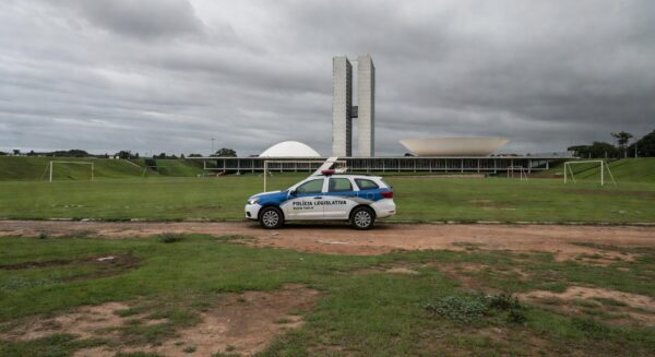 Viatura da polícia legislativa em rua de Brasília com cena de crime ao fundo, destacando escalada de violência no DF.