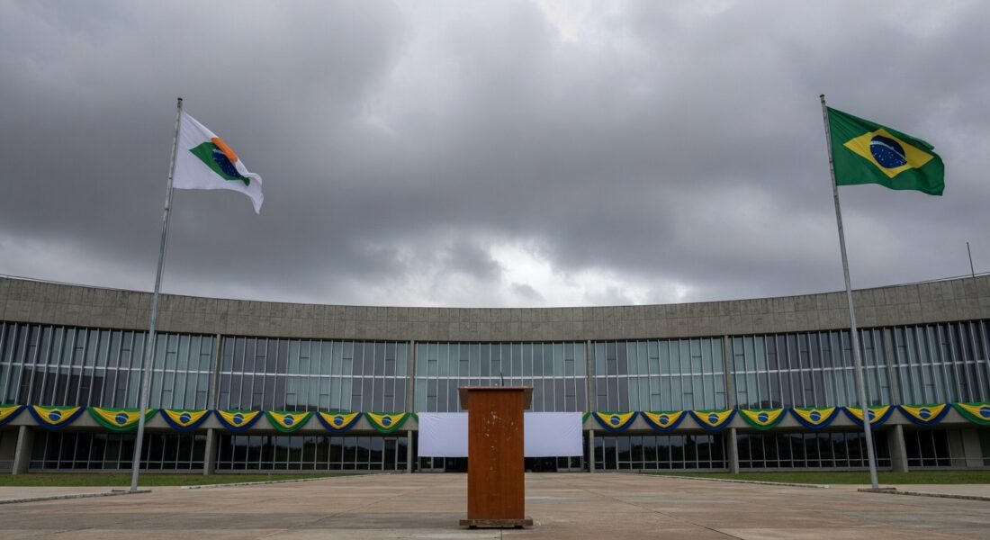 Fachada da Câmara Legislativa do DF com bandeiras e pódio vazio, representando cerimônia cívica questionada em crise econômica.