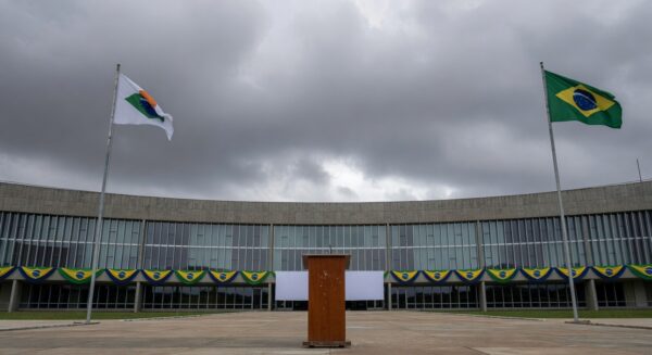 Fachada da Câmara Legislativa do DF com bandeiras e pódio vazio, representando cerimônia cívica questionada em crise econômica.