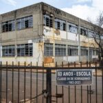 Fachada deteriorada de escola pública em Sobradinho, DF, com placa de 60 anos, destacando crise na educação.
