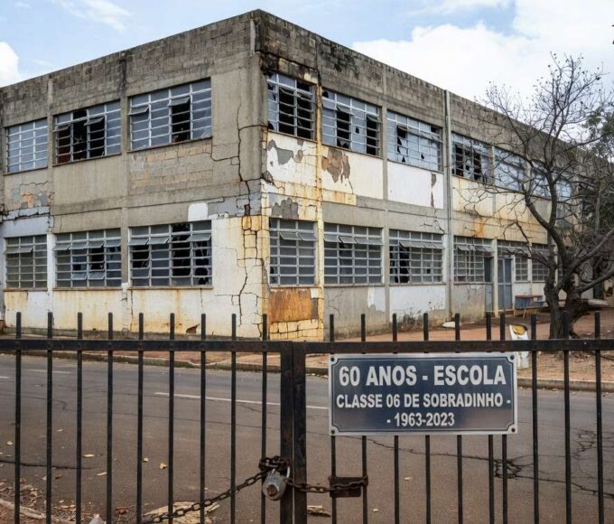 Fachada deteriorada de escola pública em Sobradinho, DF, com placa de 60 anos, destacando crise na educação.