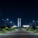 Avenida noturna em Brasília iluminada por postes de LED modernos, representando a modernização da iluminação pública no DF.