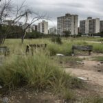 Parque Central de Águas Claras negligenciado, com grama alta, bancos quebrados e lixo, expondo negligência urbana em Brasília.
