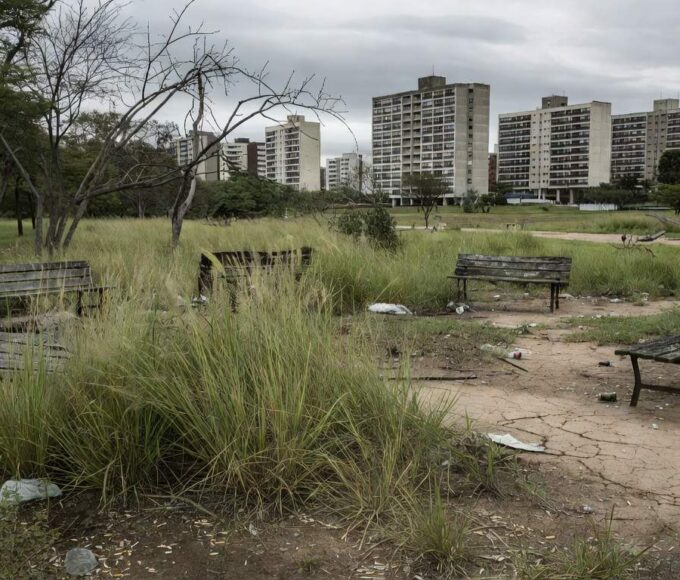 Parque Central de Águas Claras negligenciado, com grama alta, bancos quebrados e lixo, expondo negligência urbana em Brasília.