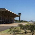 Aeroporto de Brasília com arquitetura moderna e aviões na pista, representando leilão governamental.