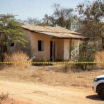 Cena de crime em residência em Águas Lindas, Goiás, com fita de isolamento policial e viatura da PM.