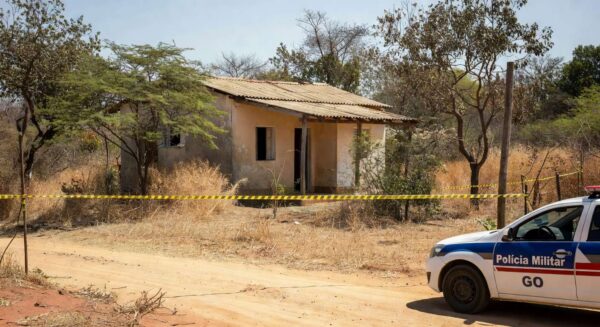 Cena de crime em residência em Águas Lindas, Goiás, com fita de isolamento policial e viatura da PM.